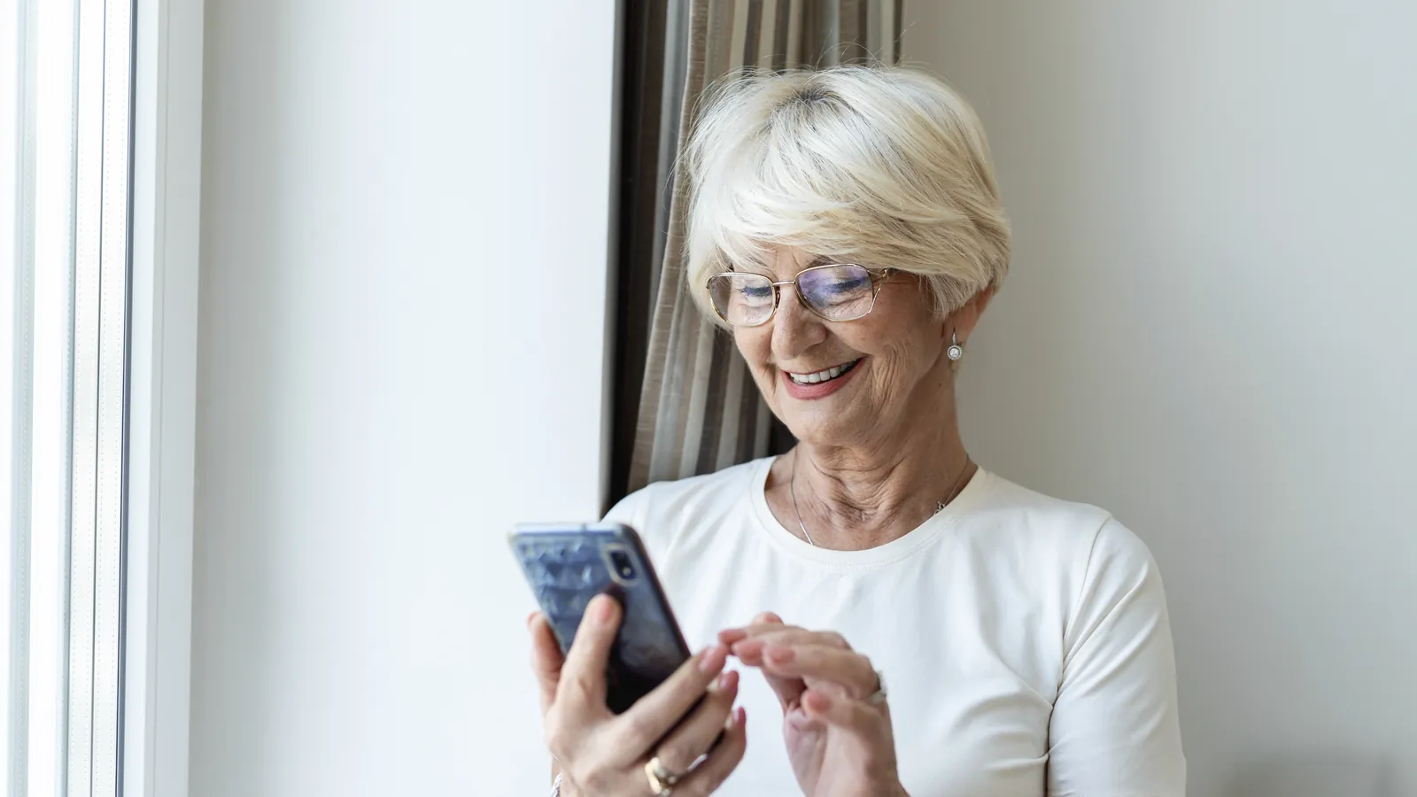 Mujer mayor sonriente leyendo una conversación de WhatsApp en su móvil en casa