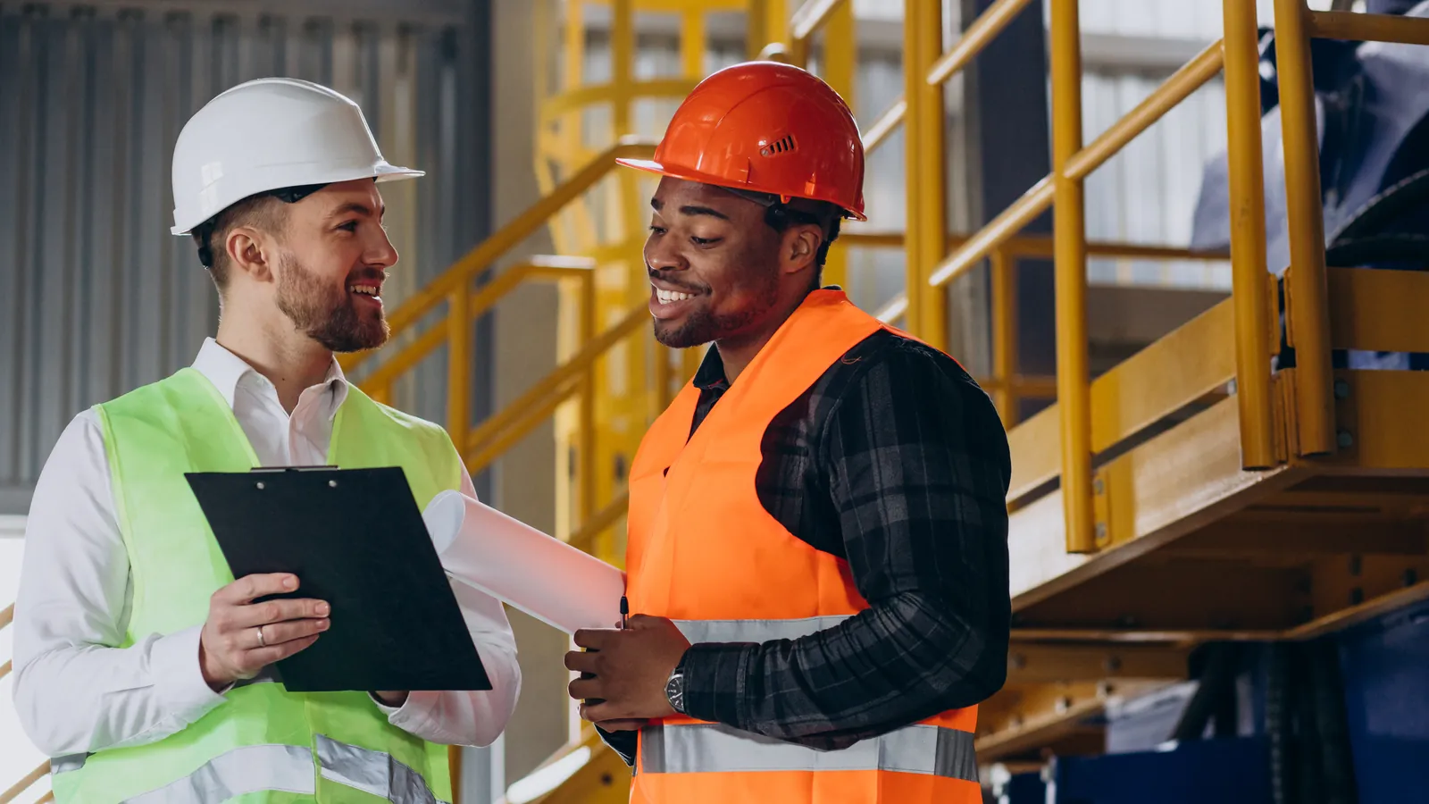Perito de accidentes laborales con carpeta conversando amigablemente con un trabajador en una nave industrial