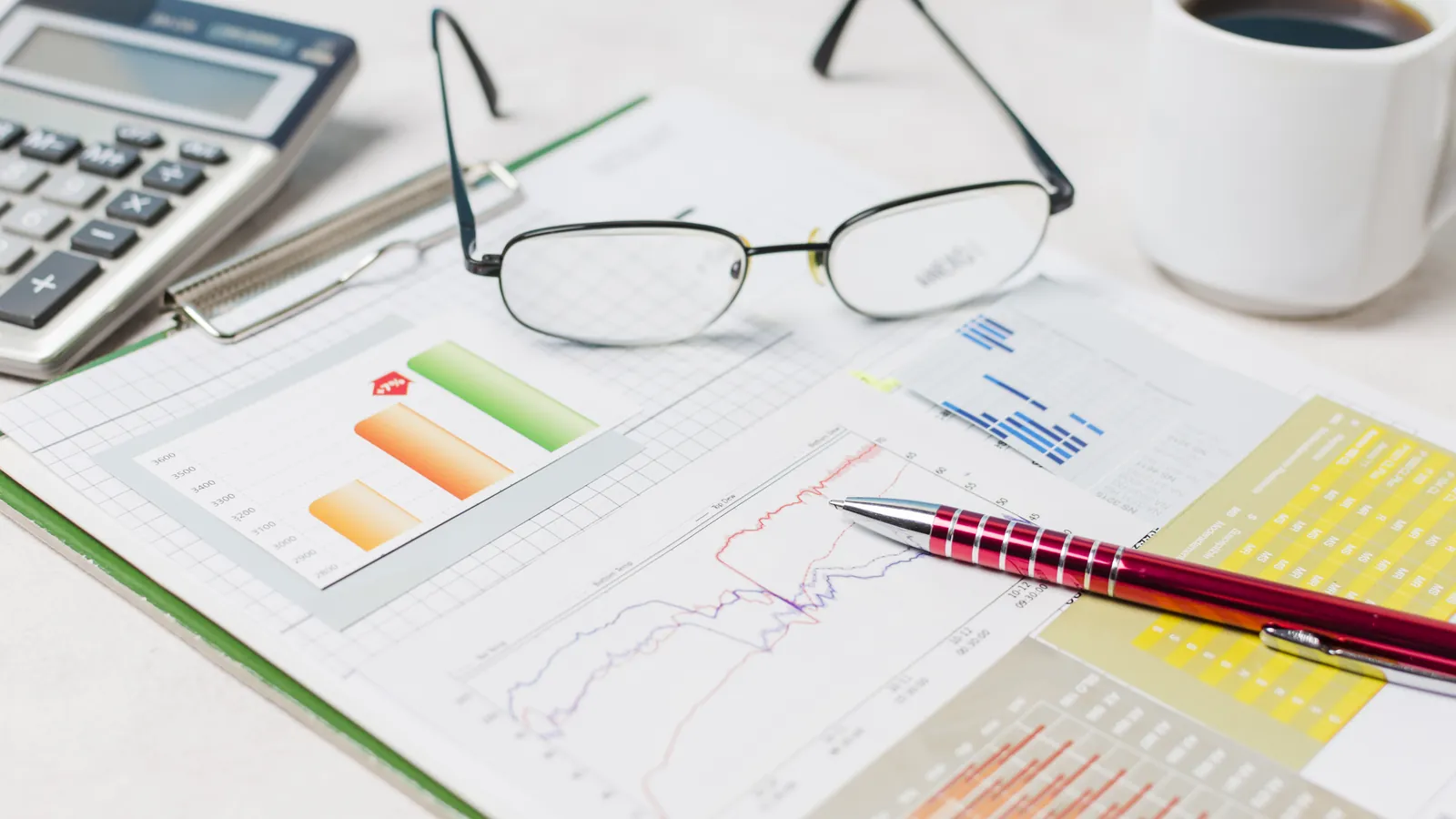 Calculadora, gafas y gráficos financieros sobre la mesa de trabajo de un economista