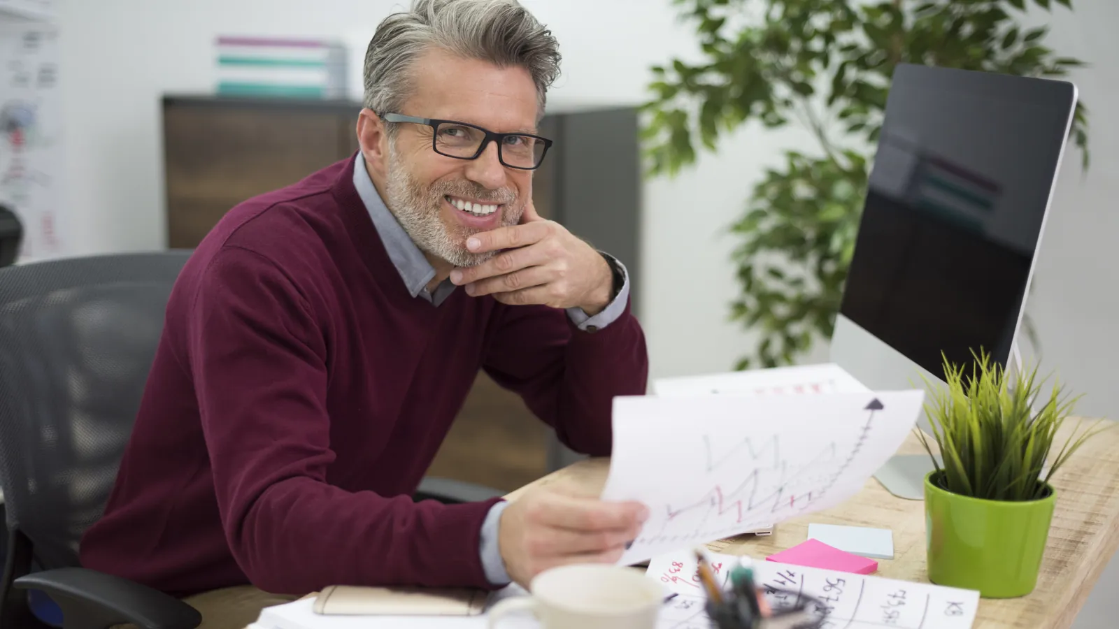 Perito economista sonriente revisando un gráfico financiero en su despacho