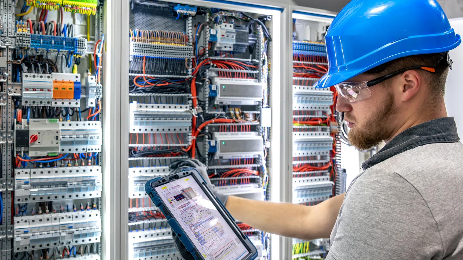 Técnico con tableta inspeccionando el cableado de un cuadro eléctrico industrial