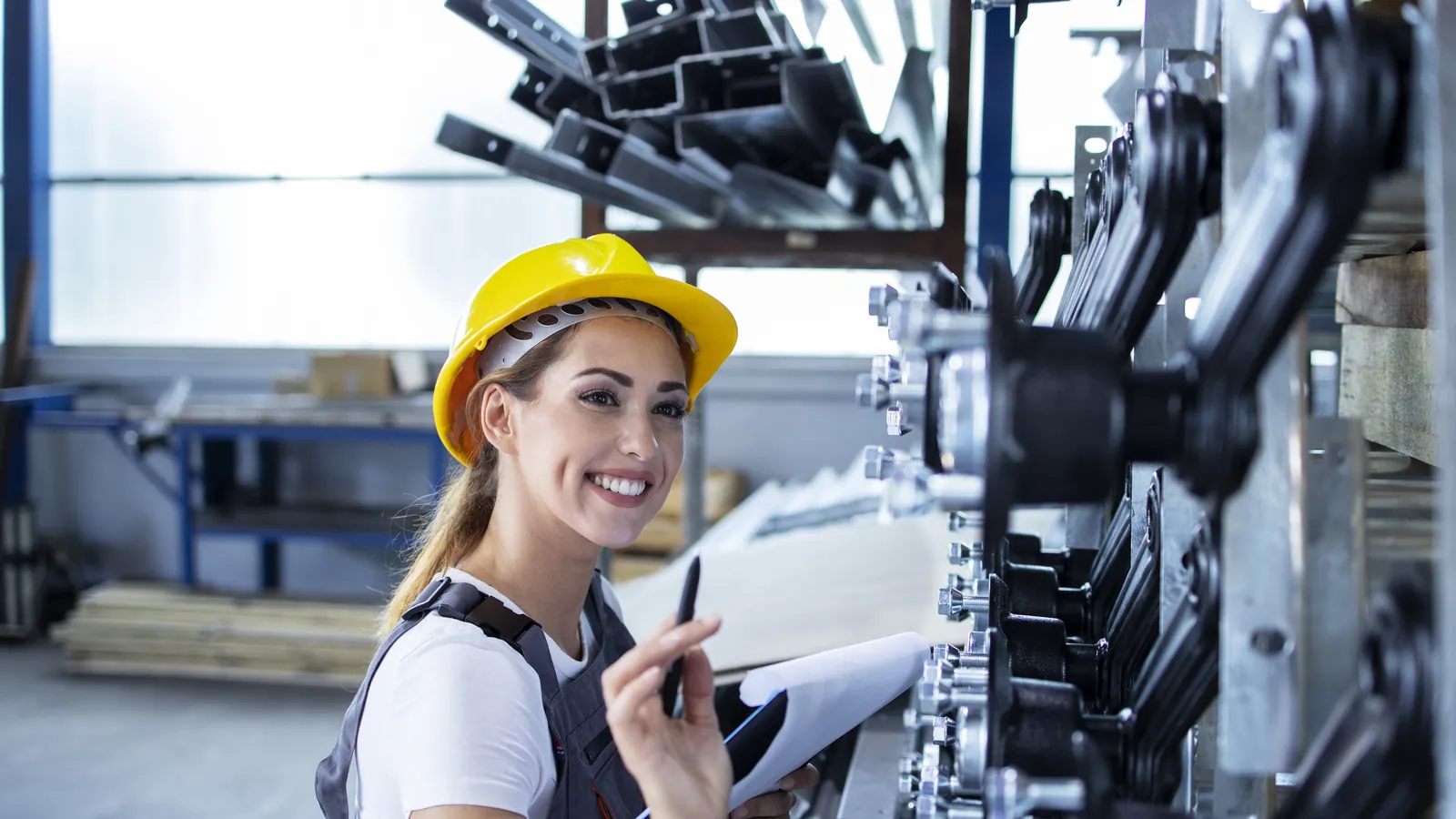 Perito industrial sonriente, con casco, revisando la maquinaria de una fábrica luminosa