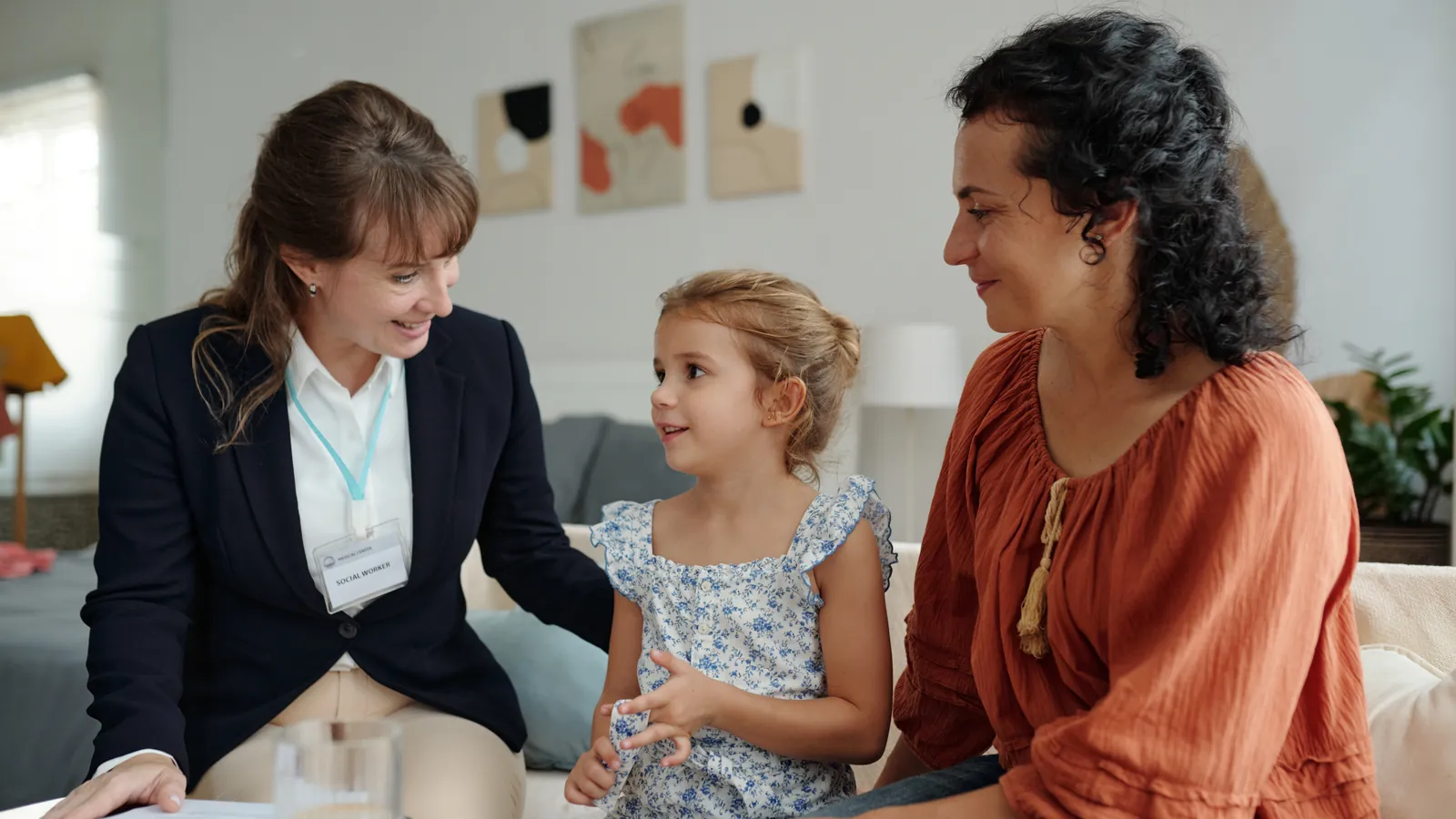 Perito social conversando en el sofá de casa con una madre y su hija pequeña