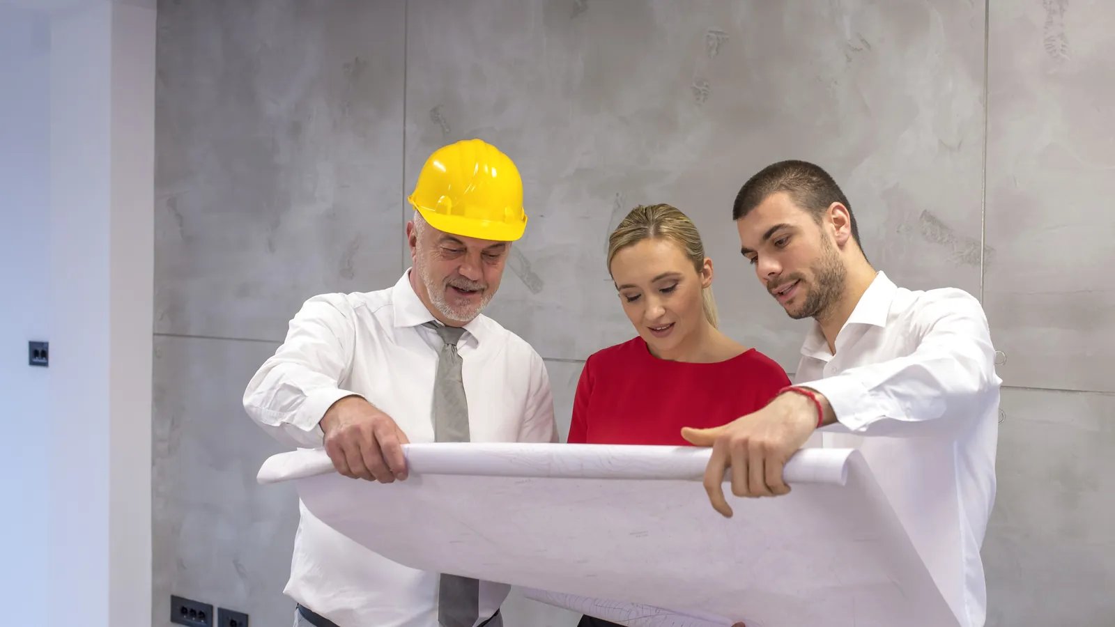 Arquitecto con casco mostrando los planos de la vivienda a una pareja de propietarios