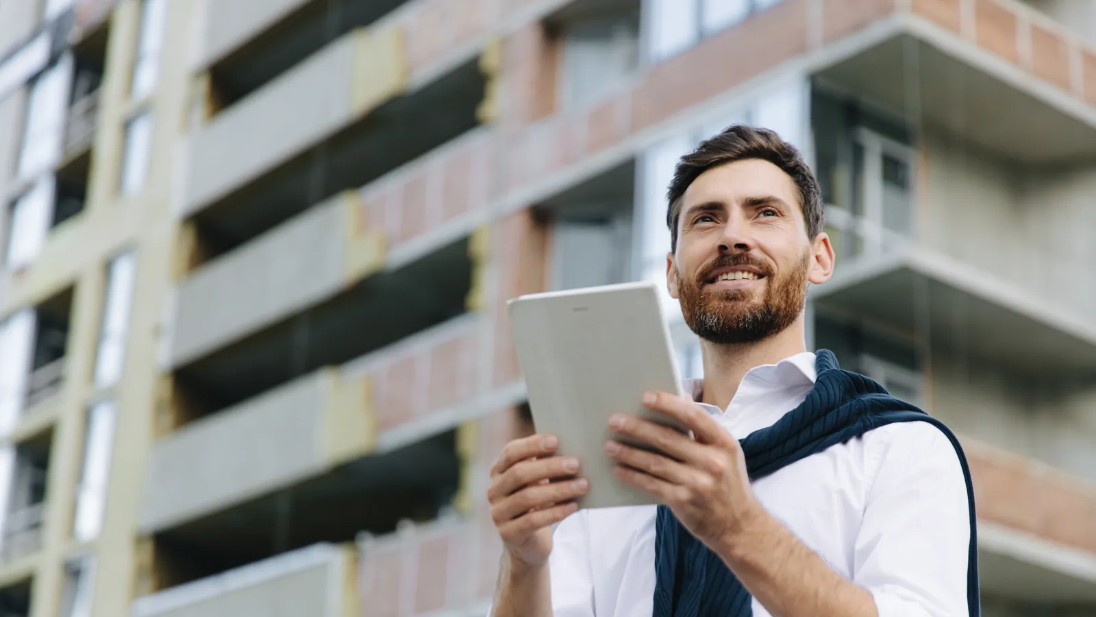 Perito arquitecto con una tableta revisando la fachada de un edificio de viviendas