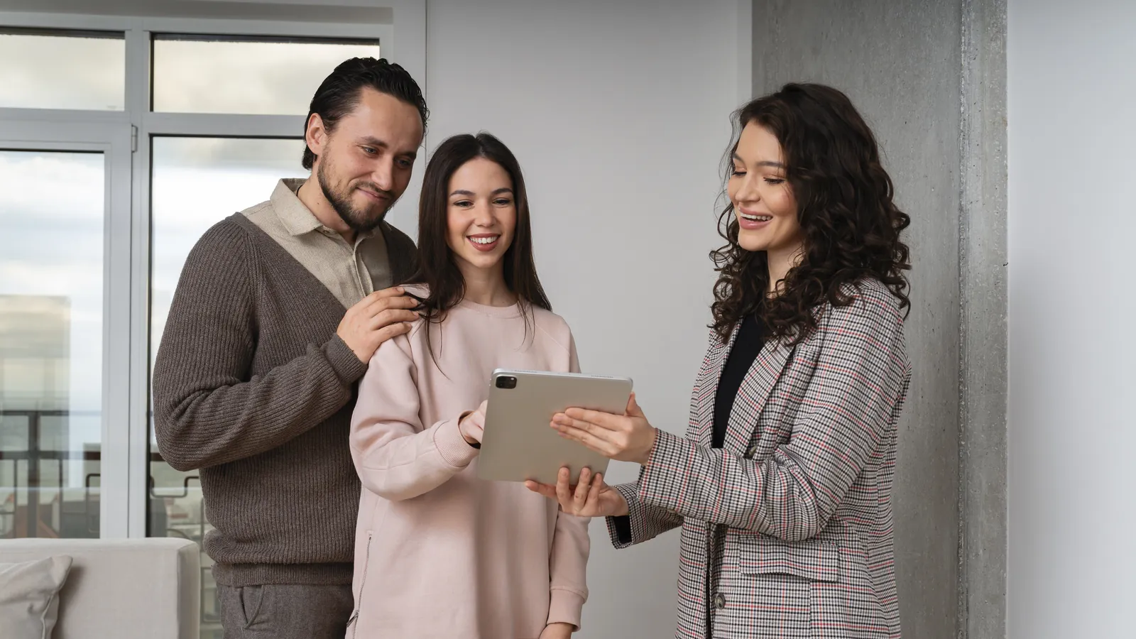 Tasadora enseñando en una tableta el plano del piso a una pareja sonriente